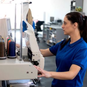 Female worker working on embroidery machine in printing factory