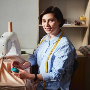 Clothes design specialist with a measuring tape wrapped around her neck pulling out a pin